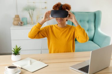 Evde sanal gerçeklik metavers VR gözlüğü takan Afro-Amerikalı genç bir kadın. Kız sanal gerçeklik kaskı takıyor. Teknoloji simülasyonu yüksek teknoloji video oyunu konsepti