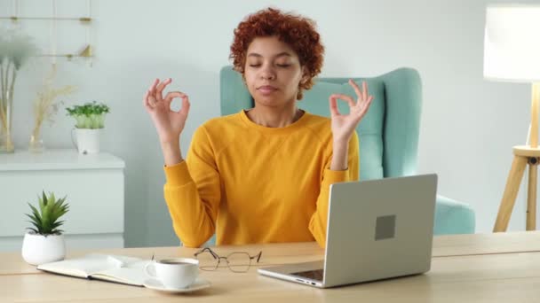 ヨガマインドフルネス瞑想 ストレスは落ち着かない 自宅のオフィスでヨガを練習アフリカの女の子 ゆったりとした室内を瞑想オフィステーブルで蓮のポーズをとる女 仕事で呼吸の練習をしている女の子 — ストック動画