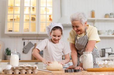Mutfakta mutlu bir aile. Büyükannem ve torunum mutfakta birlikte yemek pişiriyorlar. Küçük kıza hamur yoğurmayı öğreten büyükanne kurabiye pişiriyor. Ev işi aile oluşturma kavramına yardımcı oluyor