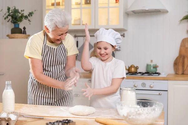 Happy family in kitchen. Grandmother and granddaughter child cook in kitchen together. Grandma teaching kid girl knead dough bake cookies. Household teamwork helping family generations concept