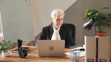 Confident stylish european middle aged senior woman using laptop at workplace. Stylish older mature 60s gray haired lady businesswoman sitting at office table. Boss leader teacher professional worker