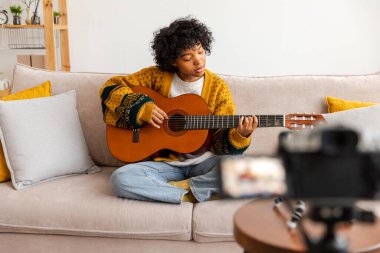 Blogger gitaristi. Gitar çalan Afrikalı Amerikalı kız blogcu webcam kayıt vlog 'uyla konuşuyor. Sosyal medya etkisinde olan kadın evde yaşıyor. Müzik içeriği yaratıcısı özel yayın