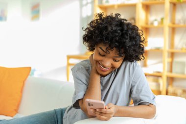 African girl holding smartphone touch screen typing scroll page at home. Woman with cell phone surfing internet using social media apps playing game. Shopping online Internet news cellphone addiction
