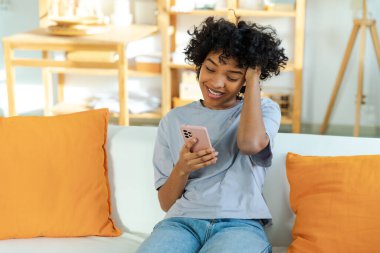 African girl holding smartphone touch screen typing scroll page at home. Woman with cell phone surfing internet using social media apps playing game. Shopping online Internet news cellphone addiction