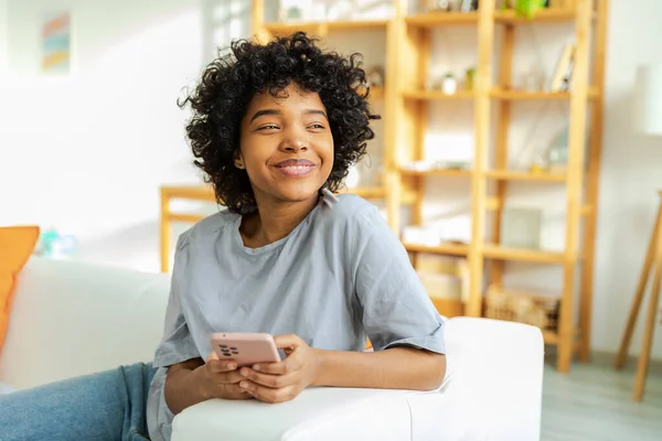 stock image African girl holding smartphone touch screen typing scroll page at home. Woman with cell phone surfing internet using social media apps playing game. Shopping online Internet news cellphone addiction