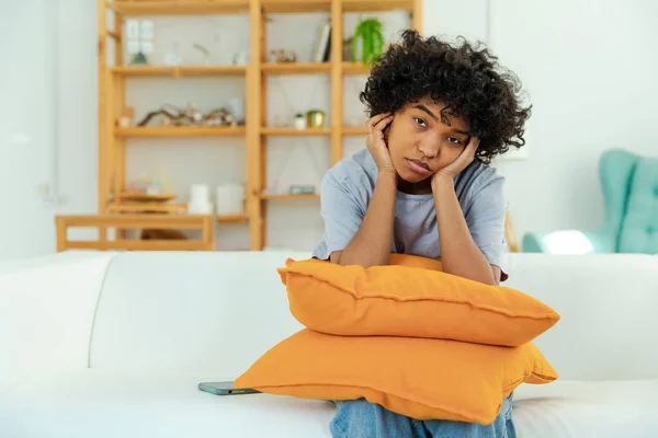 stock image African american sad thoughtful pensive unmotivated girl sitting on sofa at home indoor. Young african woman ponder look tired after long day. Girl feels depressed offended lonely upset heartbreak