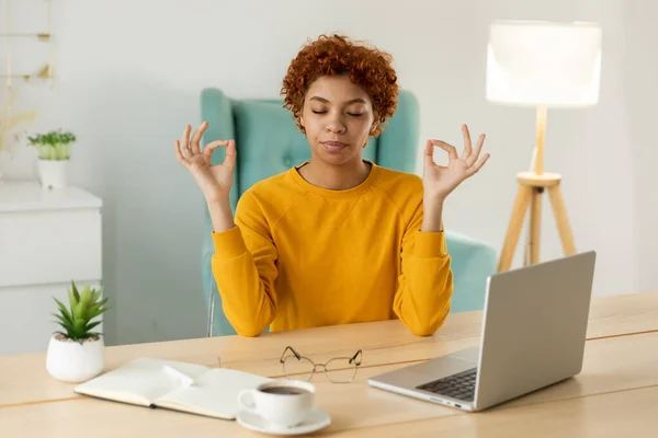 No stress keep calm. Mindful african businesswoman practices breathing exercises at home office. Peaceful young woman at workplace enjoy yoga eyes closed hands in chin mudra gesture. Office meditation