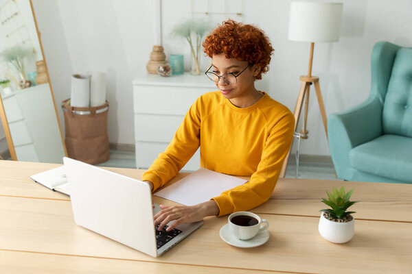 Африканская американка использует ноутбук в домашнем офисе, смотрит на экран, печатает чаты, пишет электронную почту. Молодая женщина проводит виртуальную встречу онлайн чат видео-конференции. Обучение работе на дому