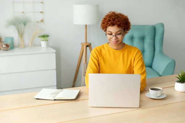 stock image African american girl using laptop at home office looking at screen typing chatting reading writing email. Young woman having virtual meeting online chat video call conference. Work learning from home