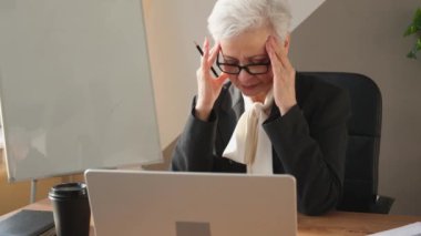 Ofiste stres yaşayan orta yaşlı, yaşlı bir kadın tapınaklara dokunuyor. Yaşlı ve olgun lider, çalışmaktan bıktı. Baş ağrısı çekiyor. Uzun dizüstü bilgisayar görme sendromu. Ofis sendromu