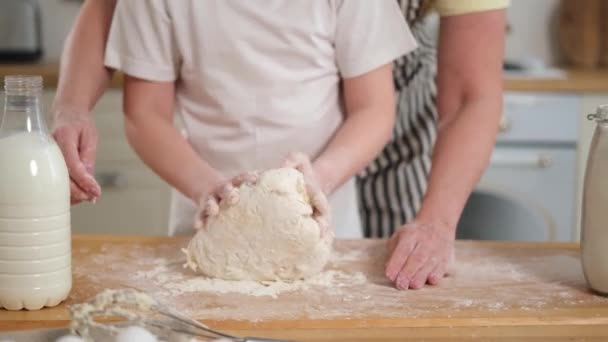 キッチンで幸せな家族 祖母の孫娘の子供の手は一緒に台所のテーブルの上で生地をこねる おばあちゃんが子供にクッキーを焼く 家族世代のコンセプトを支援する家庭のチームワーク — ストック動画