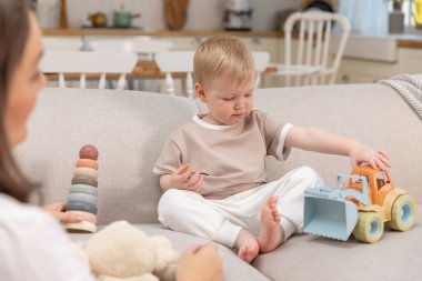 Evde mutlu bir aile. Anne ve bebek evdeki kanepede oyuncaklarla oynuyor. Küçük çocuk ve bebek bakıcısı birlikte eğleniyorlar. Genç kadın, anne, çocuk oturma odasında dinleniyor.