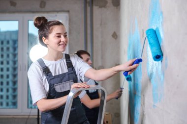 Ev dekorasyonu yenileme konsepti. Yeni ev boyama duvarının boş odasında birlikte mutlu bir çift. Karı koca ellerinde boya rulosu tutuyorlar. Yeni evde duvarları mavi boyayla boyuyorlar.