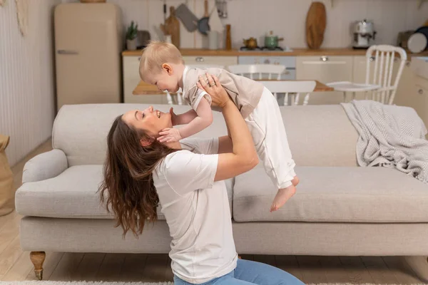 stock image Happy family at home. Mother lifting in air little toddler child son. Mom and baby boy playing having fun together at home. Mother hugs baby with love care. Young mother kid son rest in living room