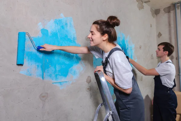 stock image Couple in new home during repair works painting wall together. Happy family holding paint roller painting wall with blue color paint in new house. Home renovation DIY renew home concept