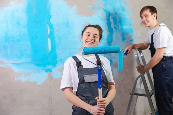 Couple in new home during repair works painting wall together. Happy family holding paint roller painting wall with blue color paint in new house. Home renovation DIY renew home concept