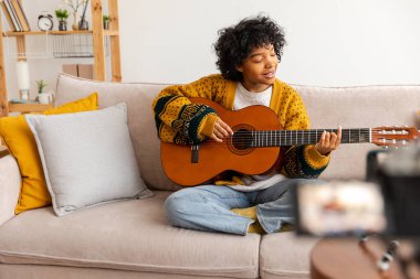 Blogger gitaristi. Gitar çalan Afrikalı Amerikalı kız blogcu webcam kayıt vlog 'uyla konuşuyor. Sosyal medya etkisinde olan kadın evde yaşıyor. Müzik içeriği yaratıcısı özel yayın