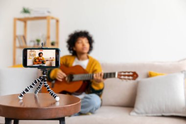 Blogger guitarist. African american girl blogger playing guitar talking to webcam recording vlog. Social media influencer woman streaming at home indoors. Music content creator broadcast tutorial