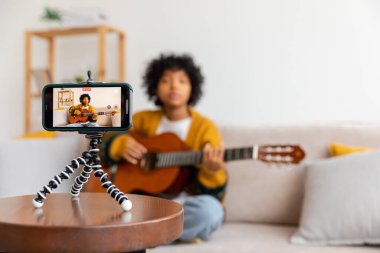Blogger gitaristi. Gitar çalan Afrikalı Amerikalı kız blogcu webcam kayıt vlog 'uyla konuşuyor. Sosyal medya etkisinde olan kadın evde yaşıyor. Müzik içeriği yaratıcısı özel yayın