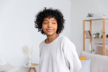 Evinde afro saç stili olan güzel Afro-Amerikalı kız. Oturma odasında kıvırcık saçlı Afrikalı genç bir kadın. Güzel etnik insanlar, ev hayatı kavramı