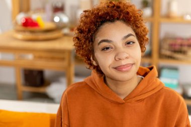 Beautiful african american girl with afro hairstyle smiling sitting on sofa at home indoor. Young african woman with curly hair smiling. Freedom happiness carefree happy people concept