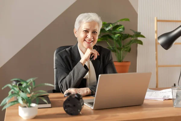 stock image Portrait of confident stylish european middle aged senior woman at workplace. Stylish older mature 60s gray haired lady businesswoman sitting in modern office. Boss leader teacher professional worker