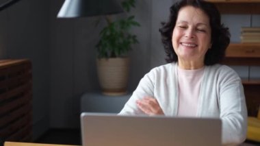 Evde dizüstü bilgisayar kullanan kendine güvenen Avrupalı orta yaşlı bir kadın. Yaşlı, şık 60 'lı yaşlarda bir kadın masada oturmuş bilgisayar ekranına bakıyor daktilo yazarak sohbet ediyor e-posta yazıyor.
