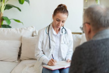 Doktor muayenehanesinde ya da evde yaşlı bir adamı muayene eden kadın doktor. Yaşlı hasta ve doktorun hastane odasında muayeneleri var. Tıbbi sağlık hizmetleri sağlık kontrolü. Doktoru ziyaret et.
