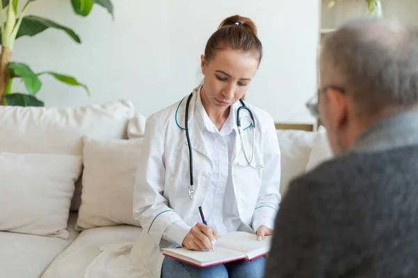 stock image Female doctor examining older senior man in doctor office or at home. Old man patient and doctor have consultation in hospital room. Medicine healthcare medical checkup. Visit to doctor