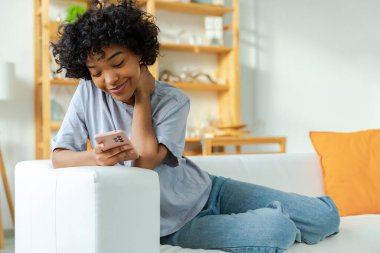 African girl holding smartphone touch screen typing scroll page at home. Woman with cell phone surfing internet using social media apps playing game. Shopping online Internet news cellphone addiction