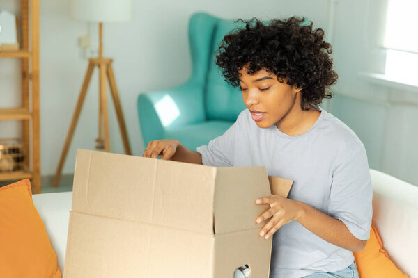 African girl unpacking delivery looking in box. Happy woman opening carton box. Female getting parcel looking at delivered goods items. Satisfied client positive feedback quick express deliver
