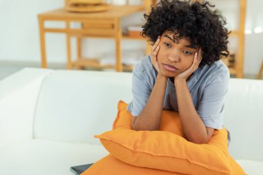 Afro-amerikan üzgün, düşünceli, düşünceli, motivasyonsuz kız evdeki kanepede oturuyor. Genç Afrikalı kadın uzun bir günün ardından yorgun görünüyor. Kız kendini üzgün hissediyor. Yalnız, üzgün, üzgün.