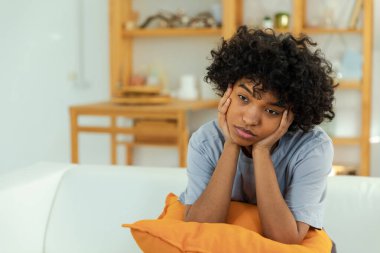 African american sad thoughtful pensive unmotivated girl sitting on sofa at home indoor. Young african woman ponder look tired after long day. Girl feels depressed offended lonely upset heartbreak