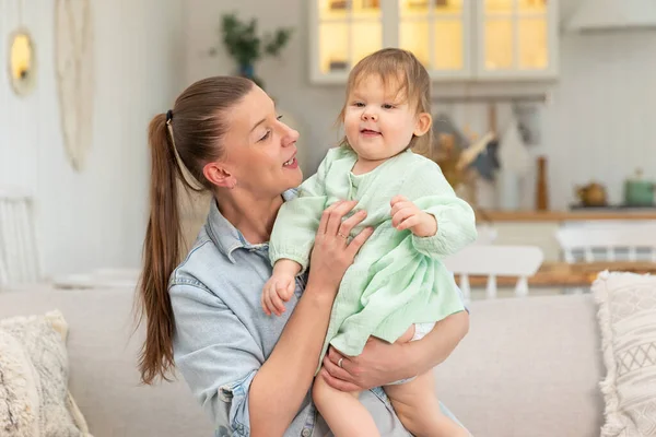 stock image Happy family at home. Mother lifting in air little toddler child daughter. Mom and baby girl playing having fun together at home. Mother hugs baby with love care. Young mother kid rest in living room