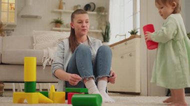 Evde mutlu bir aile. Anne ve bebek evde oyuncak küplerle oynuyorlar. Küçük çocuk ve bebek bakıcısı birlikte eğleniyorlar. Genç kadın anne, küçük kız oturma odasında dinleniyor.