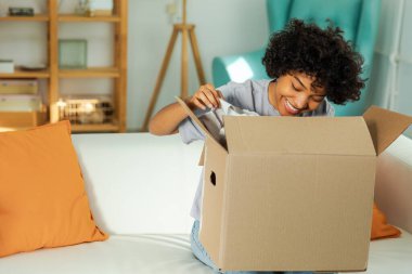 Paketleri açan Afrikalı kız kutuya bakıyor. Kutuyu açan mutlu kadın. Paket teslim edilen eşyalara bakan bir kadın. Tatmin olmuş istemci olumlu geri bildirim hızlı teslimatı