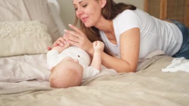 Evde mutlu bir aile. Anne, küçük bebekle yatakta oynuyor. Anne bebek birlikte oynayıp rahatlıyor. Anne bebeğe sevgiyle bakar. Bebeği emziren anne oturma odasında dinleniyor.