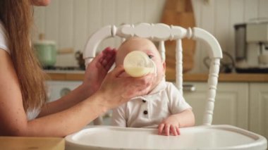 Evde mutlu bir aile. Anne, küçük bebeğini mutfaktaki şişeden besliyor. Yeni doğmuş kız süt içiyor. Bebek emziriyor, süt yiyor ve sandalyeye oturuyor. Bebeği emziren anne.