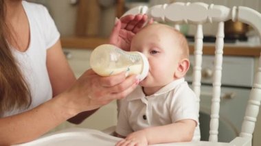 Evde mutlu bir aile. Anne, küçük bebeğini mutfaktaki şişeden besliyor. Yeni doğmuş kız süt içiyor. Bebek emziriyor, süt yiyor ve sandalyeye oturuyor. Bebeği emziren anne.