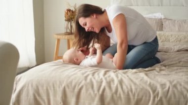 Evde mutlu bir aile. Anne, küçük bebekle yatakta oynuyor. Anne bebek birlikte oynayıp rahatlıyor. Anne bebeğe sevgiyle bakar. Bebeği emziren anne oturma odasında dinleniyor.