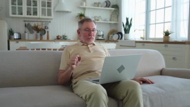 Arkadaşlarıyla video görüşmesinde dizüstü bilgisayarından konuşan mutlu orta yaşlı bir adam. Yetişkin yaşlı büyükbaba internette yetişkin çocuklarla konuşarak eğleniyor. Eski nesil modern teknoloji kullanımı