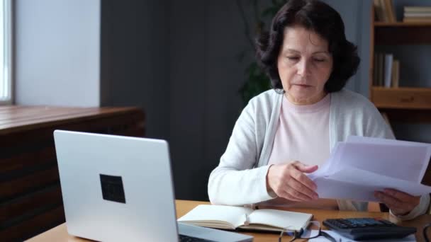 Μεσήλικη Ηλικιωμένη Γυναίκα Κάθεται Φορητό Υπολογιστή Και Χαρτί Έγγραφο Επιβλητική — Αρχείο Βίντεο