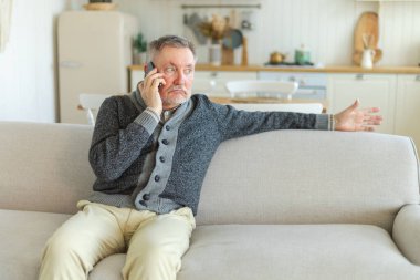 Mutlu orta yaşlı bir adam aile dostlarıyla akıllı telefondan konuşuyor. Yetişkin bir büyükbaba cep telefonuyla yetişkin çocuklarla konuşuyor, evde dinleniyor. Eski nesil modern teknoloji kullanımı