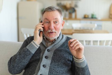 Mutlu orta yaşlı bir adam aile dostlarıyla akıllı telefondan konuşuyor. Yetişkin bir büyükbaba cep telefonuyla yetişkin çocuklarla konuşuyor, evde dinleniyor. Eski nesil modern teknoloji kullanımı