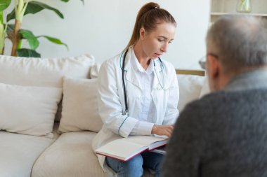 Doktor muayenehanesinde ya da evde yaşlı bir adamı muayene eden kadın doktor. Yaşlı hasta ve doktorun hastane odasında muayeneleri var. Tıbbi sağlık hizmetleri sağlık kontrolü. Doktoru ziyaret et.