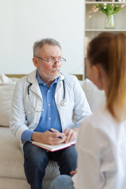 Kıdemli doktor, genç kadını muayenehanede ya da evde muayene ediyor. Kız hasta ve doktorun hastane odasında muayenesi var. Tıbbi sağlık hizmetleri sağlık kontrolü. Doktoru ziyaret et.
