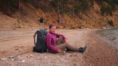 Turizm macerası yürüyüşü. Gezintiden sonra güzel manzaraya bakan sırt çantalı kadın dinleniyor. Sırt çantalı gezgin bayan turist göl kenarında oturuyor. Yürüyüşçü kadın aktif turizmin tadını çıkarıyor