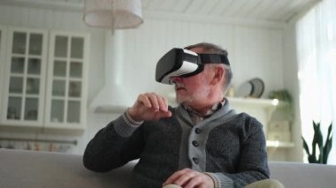 Evde sanal gerçeklik metavers VR gözlük takan heyecanlı olgun bir adam. Dedem sanal gerçeklik miğferinde sanal gerçeklik deneyimi sırasında havaya dokunuyor. Benzetim yüksek teknolojili video oyunu