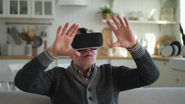 自宅でVrメガネのヘッドセットを仮想現実を使って身に着けている興奮した熟年男性 バーチャルリアリティヘルメットのVr体験中に祖父が空気に触れる シミュレーションハイテクビデオゲーム — ストック動画