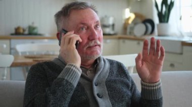 Mutlu orta yaşlı bir adam aile dostlarıyla akıllı telefondan konuşuyor. Yetişkin bir büyükbaba cep telefonuyla yetişkin çocuklarla konuşuyor, evde dinleniyor. Eski nesil modern teknoloji kullanımı